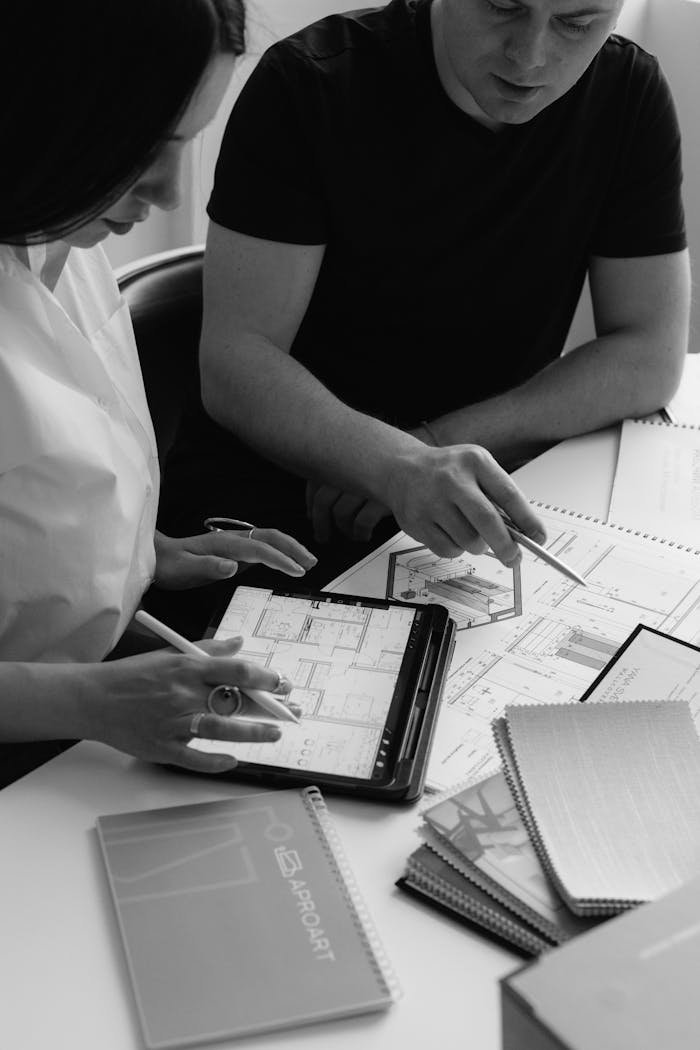 Black and white photo of architects discussing project plans using digital tablets and paper documents.